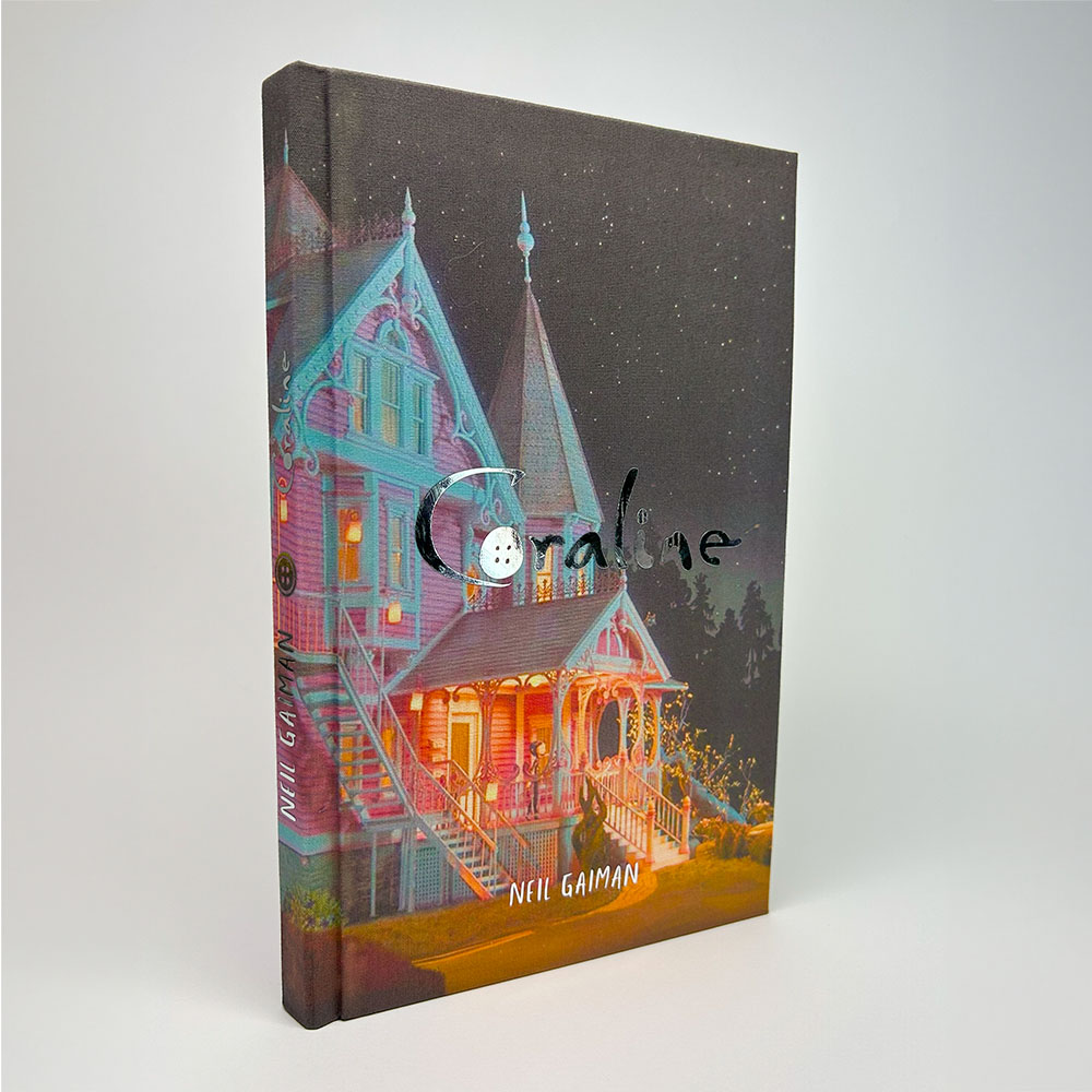 Vista frontal del libro Coraline personalizado por Skybookbindery, con la casa iluminada en tonos rosa y turquesa.